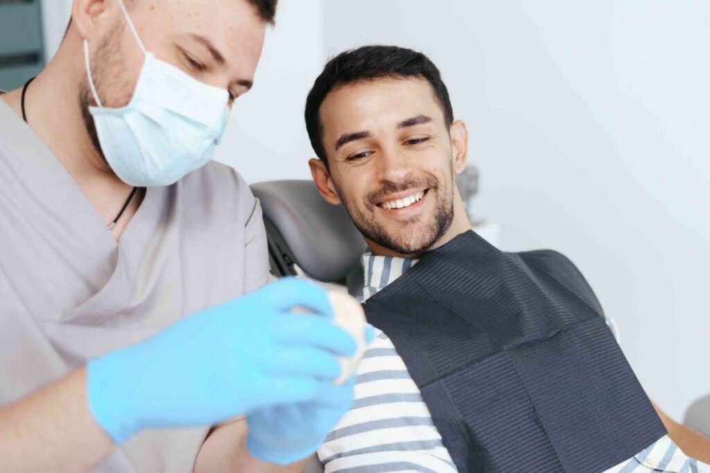 Dentist examining a smiling patient wearing a dental cover during an Invisalign consultation